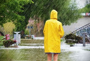 Photo of a woman in a raincoat looking at a flooded neighborhood.