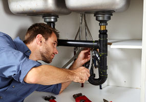 Photo of a licensed plumber inspecting the piping below a sink.