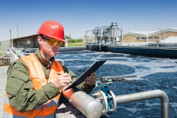 Photo of a worker with a clipboard in front of a tank of water at a water treatment facility.