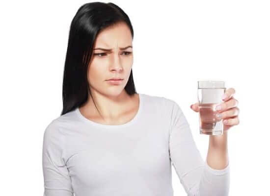 Image of a woman looking angrily at a glass of water containing lead and chromium-6