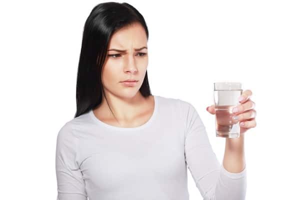 Image of a woman looking angrily at a glass of water containing lead and chromium-6