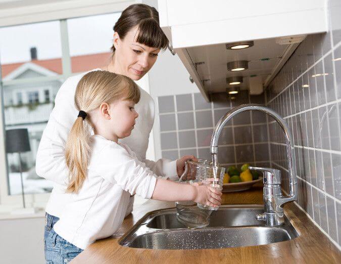 A woman and her daughter fill a glass with Chicago tap water from their faucet.
