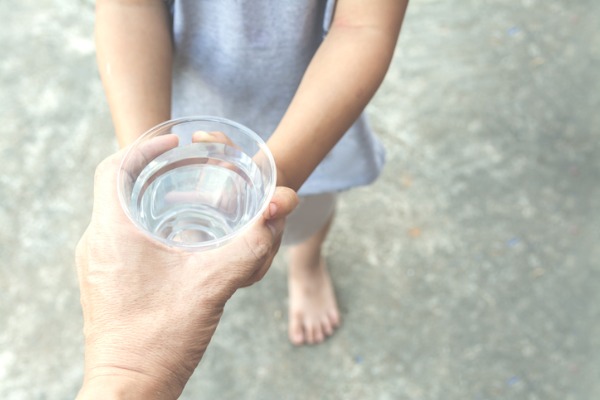 Image of a father’s hand passing a glass of clean water down to his child.