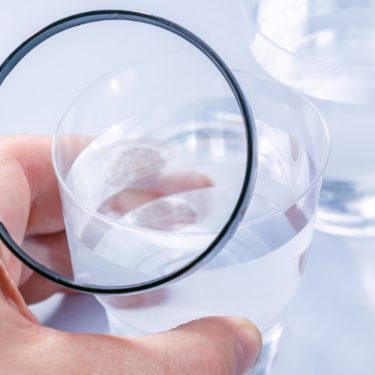 Person using a magnifying glass to examine a glass of water