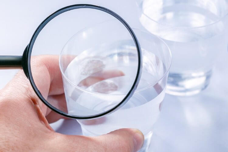 Person using a magnifying glass to examine a glass of water