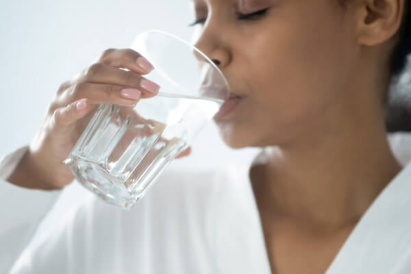 An image of a woman drinking a glass of cleaner and healthier water. 