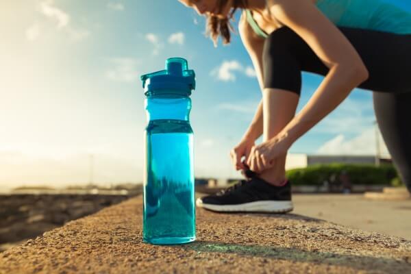 Image of a water bottle in front of a woman in workout gear tying her shoe.