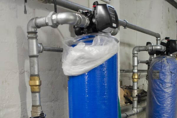 A blue water softener works in a furnace room.